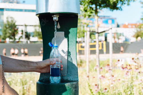 Foto Hand refilling plastic water bottle at public drinking fountain, close-up