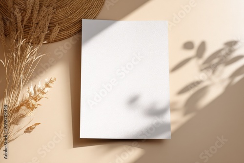 Blank white paper template with natural shadow overlay and dried grass accents on beige background