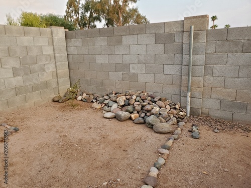 Φωτογραφία Landscaping River Rocks Piled Up Against A Cinder Block Wall in Arizona Backyard