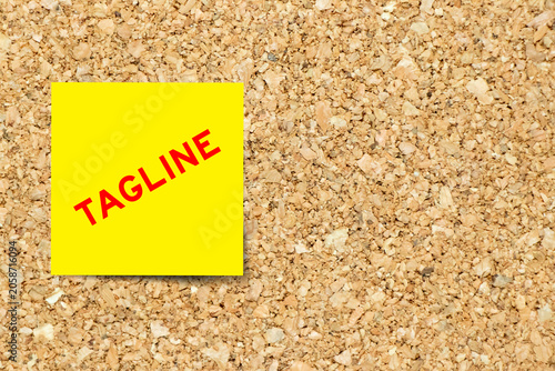 Yellow note paper with word tagline on cork board background with copy space