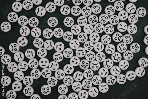 White round beads featuring various black emoticon expressions are scattered across a dark textured background.