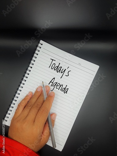 A person holds a grey pen over a spiral notebook that has the words 