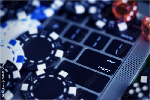 Online gambling concept with poker chips and dice scattered on a laptop keyboard. Close-up view focusing on the return and enter keys for internet betting themes background