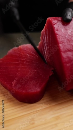 Close-up of a chef slicing fresh tuna on a wooden cutting board. Detailed view of sharp knife, raw fish texture, and professional kitchen atmosphere highlights premium culinary craftsmanship and fine 