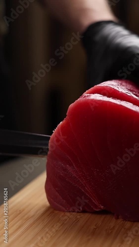 Close-up of a chef slicing fresh tuna on a wooden cutting board. Detailed view of sharp knife, raw fish texture, and professional kitchen atmosphere highlights premium culinary craftsmanship and fine 
