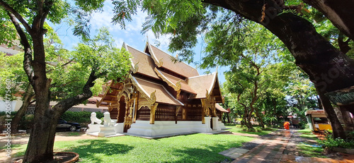 Historic Lanna-style temple architecture at Wat Phra Singh under a clear blue sky, surrounded by lush green trees in Chiang Mai, Thailand.