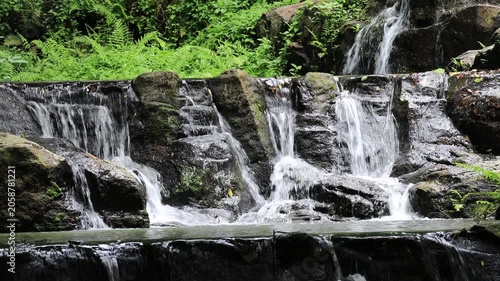 The video background features a natural landscape of a waterfall in a lush forest. Sam Lan Waterfall in Saraburi National Park boasts beautiful flowing water surrounded by diverse flora.