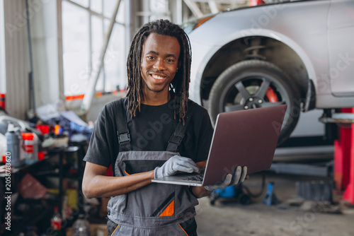 Foto Young African American man working as a mechanic, performing car diagnostics wit