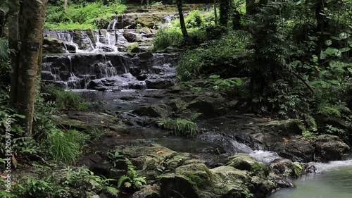 The video background features a natural landscape of a waterfall in a lush forest. Sam Lan Waterfall in Saraburi National Park boasts beautiful flowing water surrounded by diverse flora.