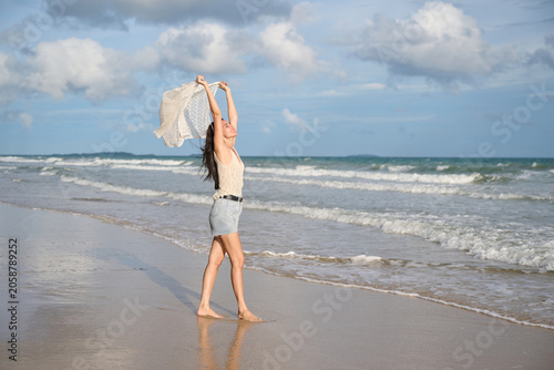 Photography Young woman with a flowing scarf joyfully embracing the ocean breeze on a sandy beach