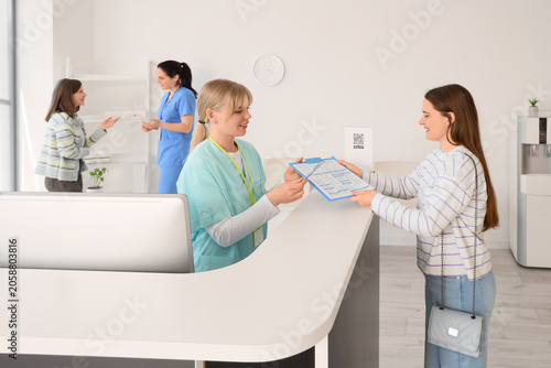 фотографія Medical receptionist handing patient clipboard with registration form at clinic