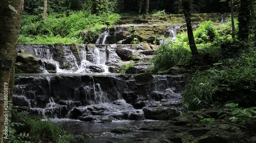 The video background features a natural landscape of a waterfall in a lush forest. Sam Lan Waterfall in Saraburi National Park boasts beautiful flowing water surrounded by diverse flora.