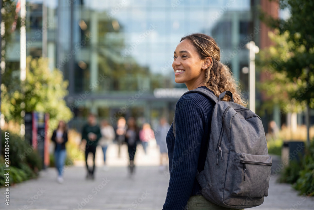 Fototapeta premium Smiling female student with backpack walking on university campus