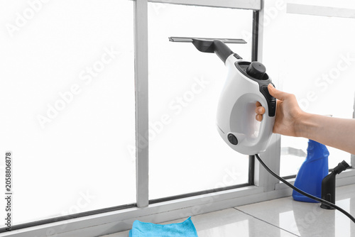 Fotografie Female hand steam cleaning window in room
