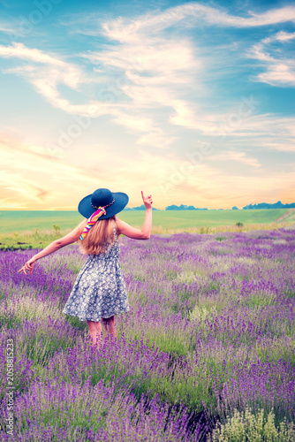 Young woman walking in blooming lavender field under cloudy sky at sunset