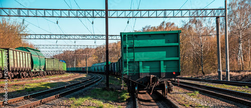Green freight train cars on railway tracks in countryside under blue sky