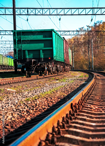 Green freight train cars on railway tracks in countryside under blue sky