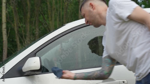 A man washes the car windows with a cloth before applying an anti-rain coating.
