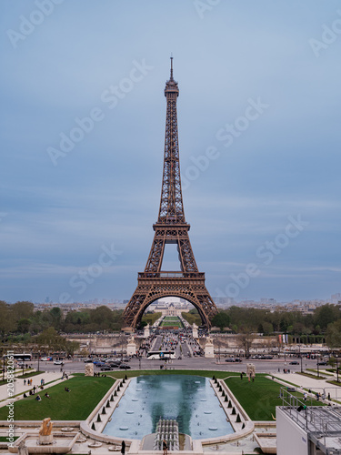 Paris, France - March 24 2026: The Eiffel Tower viewed across the Trocadero fountains under an overcast spring sky, with tourists and traffic in the Place du Trocadero.