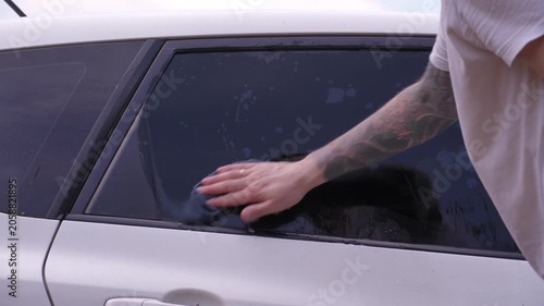 A man washes the car windows with a cloth before applying an anti-rain coating.
