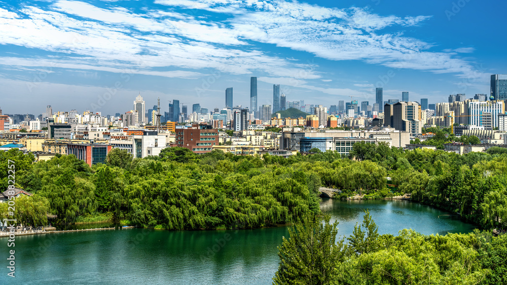 Obraz premium Urban Skyline with Green Park and Lake Under Clear Blue Sky