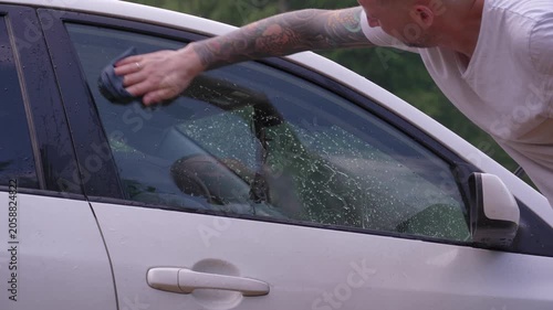 A man washes the car windows with a cloth before applying an anti-rain coating.