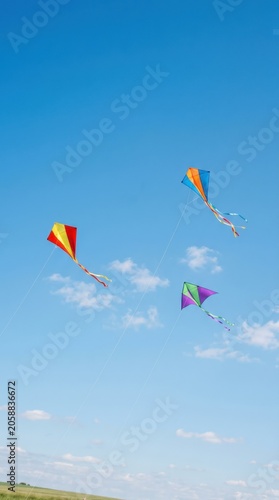Three colorful kites flying in bright blue sky. Concept for International Childrens Day celebration. Active leisure and outdoor recreation for happy kid enjoying summer holiday activity.