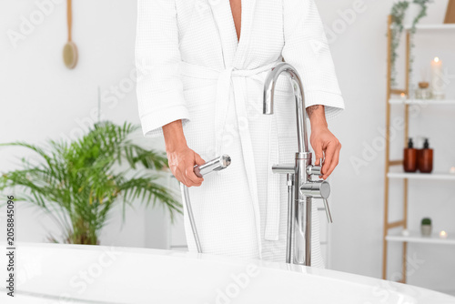 Young man running bathtub with warm water in bathroom