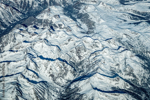 Aerial view of snow-covered mountain ridges and deep shadow-filled valleys in the Rocky Mountains, USA, photographed from cruising altitude.