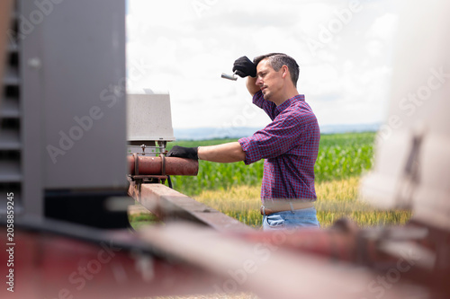 Farmer wiping sweat from forehead repairing farming machine