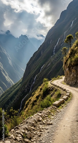 Winding mountain dirt road hugs steep, green slopes with waterfalls cascading