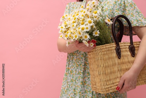 Woman with beautiful chamomile flowers in bag on pink background, closeup