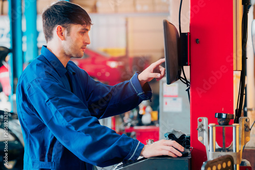 Mechanic working with computer in automotive workshop, focused male technician using diagnostic monitor in garage