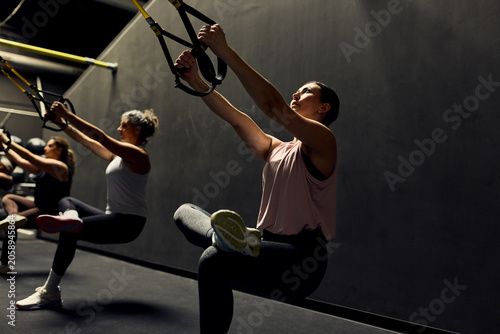 Women performing TRX suspension workout in a gym class focusing on strength, balance and core stability