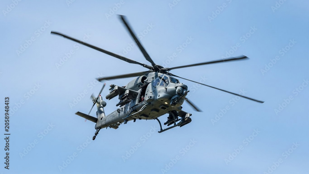 Fototapeta premium Modern combat helicopter in flight equipped with missiles and rockets under a clear blue sky during a military exercise.