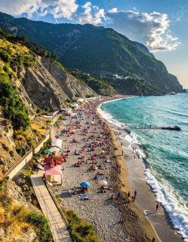 Crowded sunny beach by cliffs