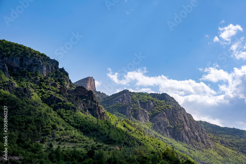 Dramatic landscape featuring rugged limestone peaks and lush green forests. High contrast lighting creates deep shadows across the pristine mountain wilderness. Majestic mountain range.