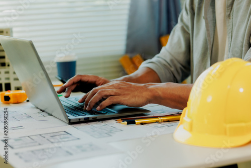 Successful Asian businessman analyzing construction blueprints and model data on laptop monitor.