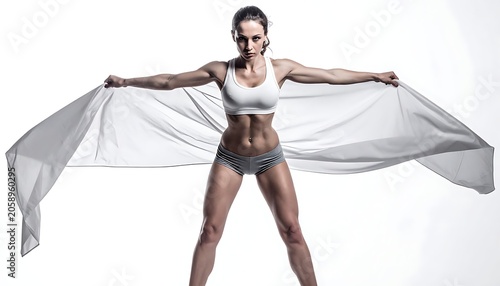 Muscular woman in workout attire holds a white fabric, arms outstretched, against a bright white background