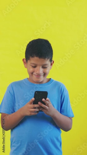 Happy little boy using smartphone on yellow background