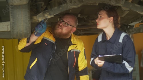 Caucasian male mechanic with glasses and a beard works alongside a female technician, reviewing a digital tablet and giving a thumbs-up. This high-energy commercial imagery represents gender diversity