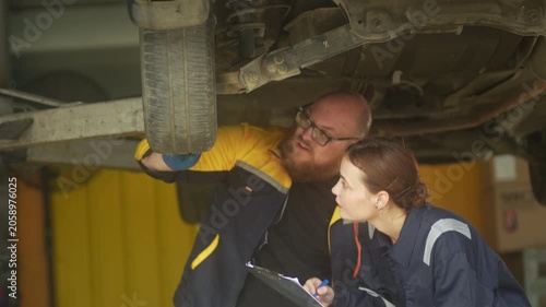 Caucasian male mechanic with glasses and a beard works alongside a female technician, reviewing a digital tablet and giving a thumbs-up. This high-energy commercial imagery represents gender diversity