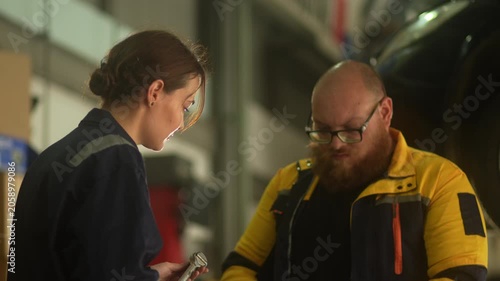Caucasian male mechanic with glasses and a beard works alongside a female technician, reviewing a digital tablet and giving a thumbs-up. This high-energy commercial imagery represents gender diversity