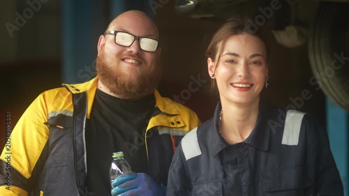 Caucasian male mechanic with glasses and a beard works alongside a female technician, reviewing a digital tablet and giving a thumbs-up. This high-energy commercial imagery represents gender diversity