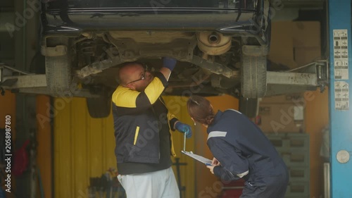 Caucasian male mechanic with glasses and a beard works alongside a female technician, reviewing a digital tablet and giving a thumbs-up. This high-energy commercial imagery represents gender diversity