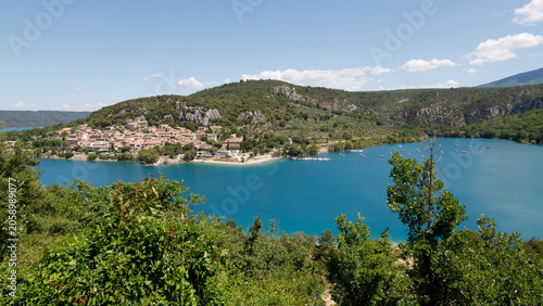 Foto Sommeridylle am Seeufer: Dorf zwischen Hügeln und Wasser.