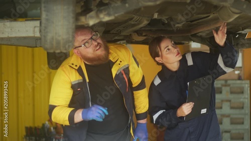 Caucasian male mechanic with glasses and a beard works alongside a female technician, reviewing a digital tablet and giving a thumbs-up. This high-energy commercial imagery represents gender diversity