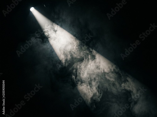 A spotlight shines through smoke in a dark room with a beam of light