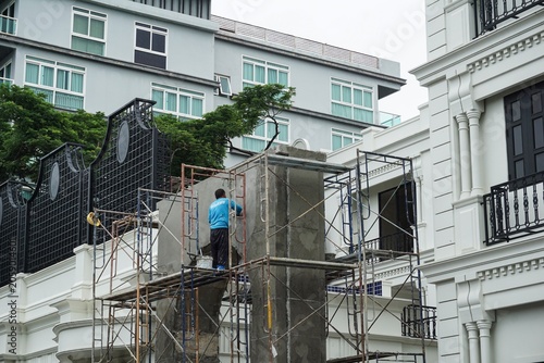 Construction worker on scaffolding plastering a concrete arch at a hotel renovation site in One Nimman, Chiang Mai, Thailand on June 14, 2026.