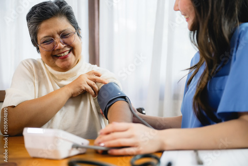 Billede på lærred Asian senior woman receiving blood pressure check doctor while young nurse using digital sphygmomanometer senior, Geriatric nursing care service routine hypertension exam, homecare service senior